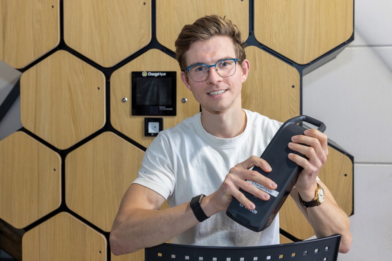 Jorg Wellink hält einen E-Bike-Akku vor einem ChargeHyve Ladeschrank mit sechseckigen Holztüren.